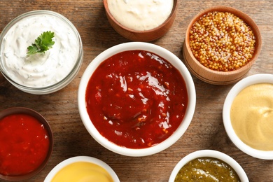 Set of different delicious sauces on wooden table, top view