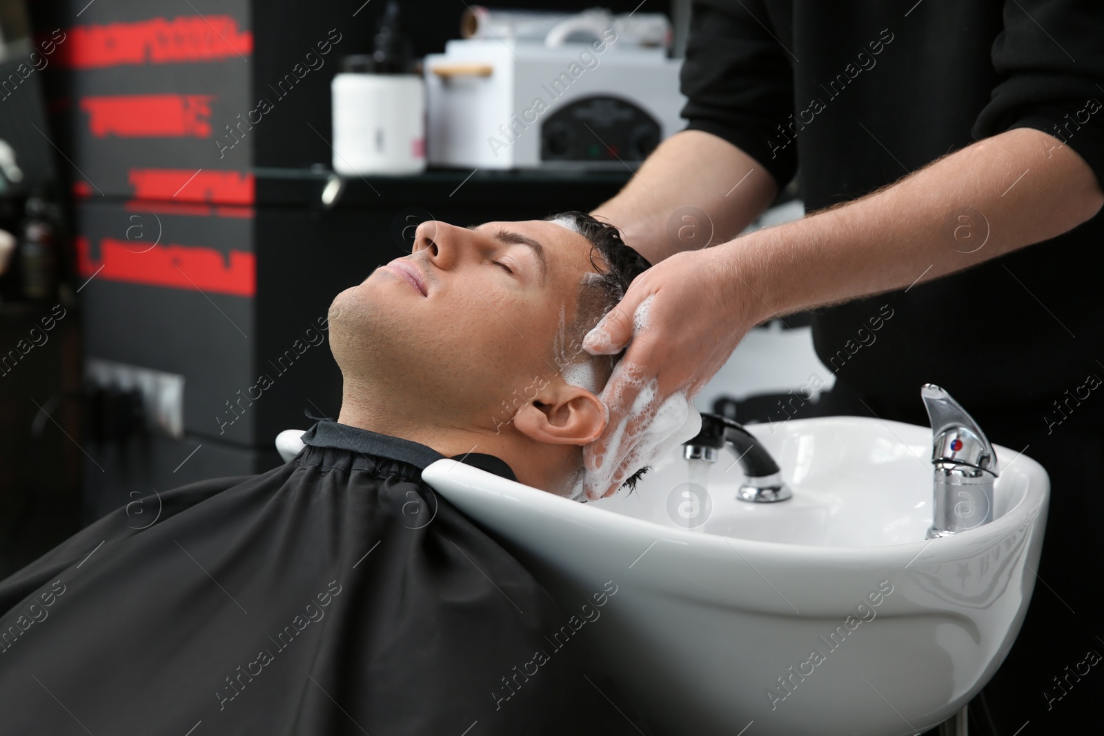 Photo of Professional barber washing client's hair at sink in salon, closeup