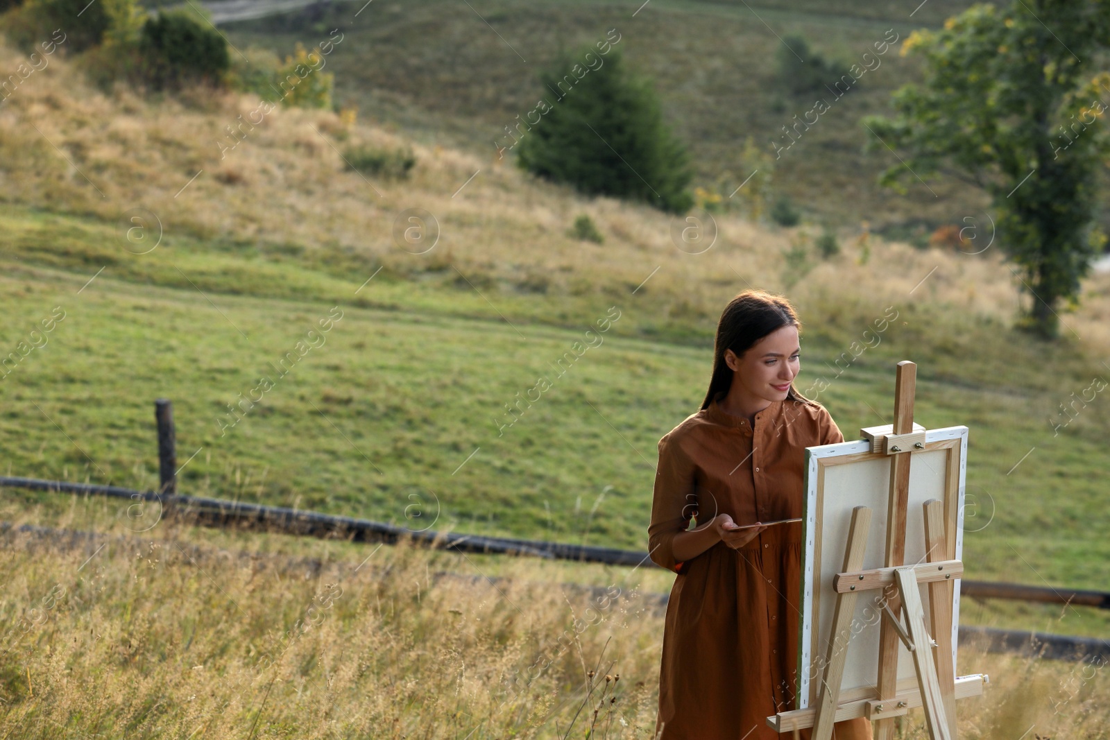 Photo of Beautiful young woman drawing on canvas in nature. Space for text