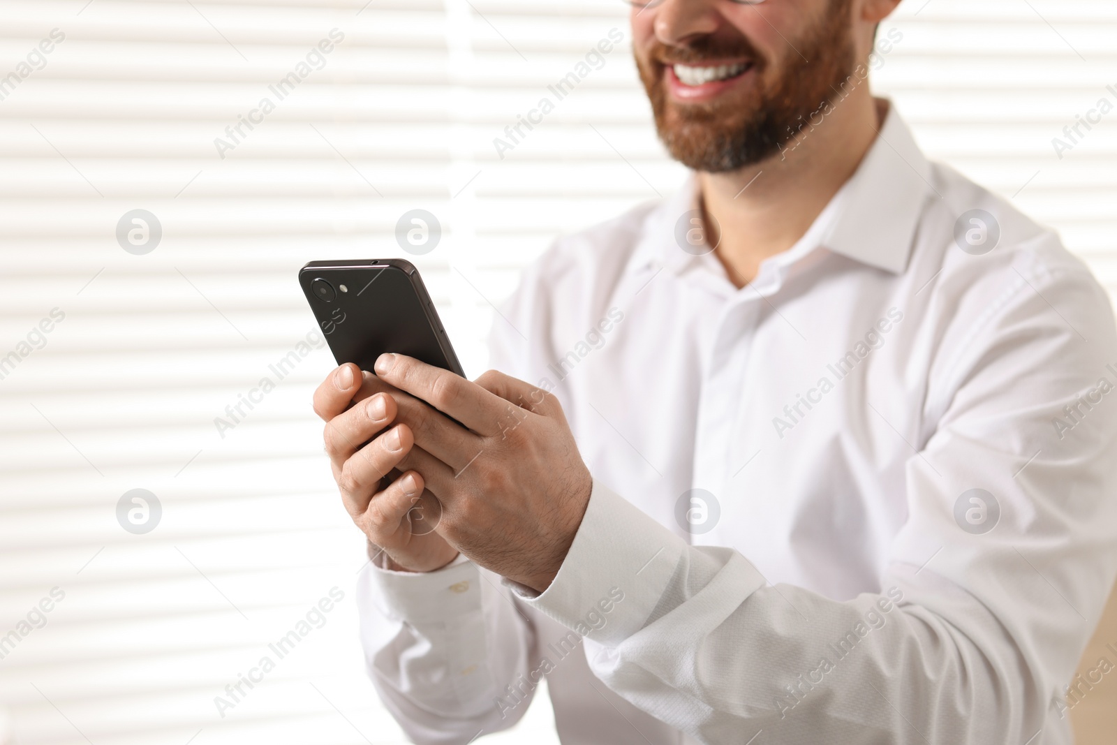 Photo of Smiling man using smartphone in office, closeup