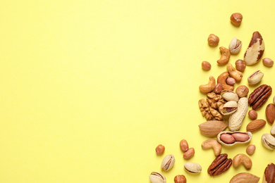 Different delicious nuts on yellow background, flat lay. Space for text