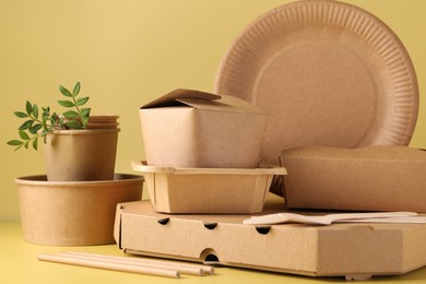 Photo of Eco friendly food packaging. Paper containers, tableware and green twigs on pale yellow background