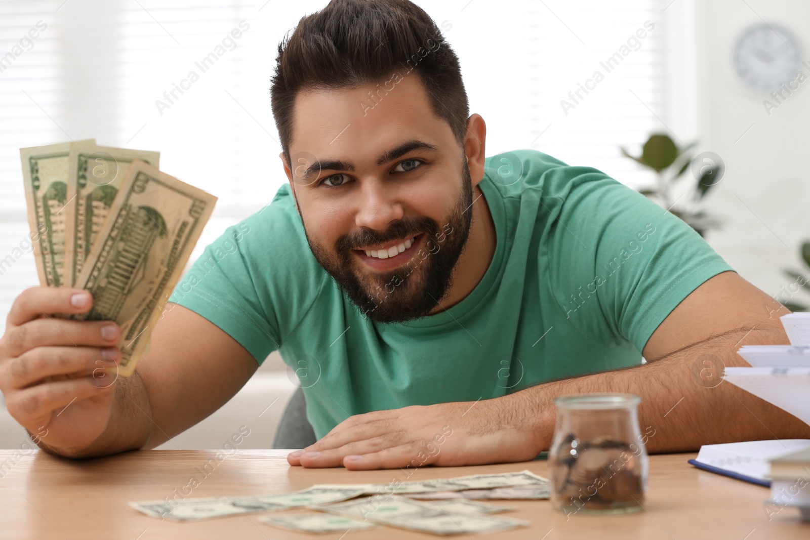Photo of Happy young man with money at wooden table indoors