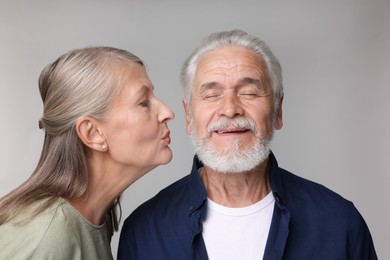Senior woman kissing her beloved man on light grey background