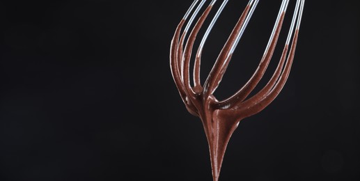 Image of Whisk with yummy chocolate cream on black background, closeup. Banner design with space for text