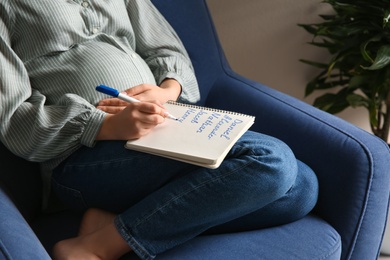 Photo of Pregnant woman with baby names list sitting in armchair, closeup
