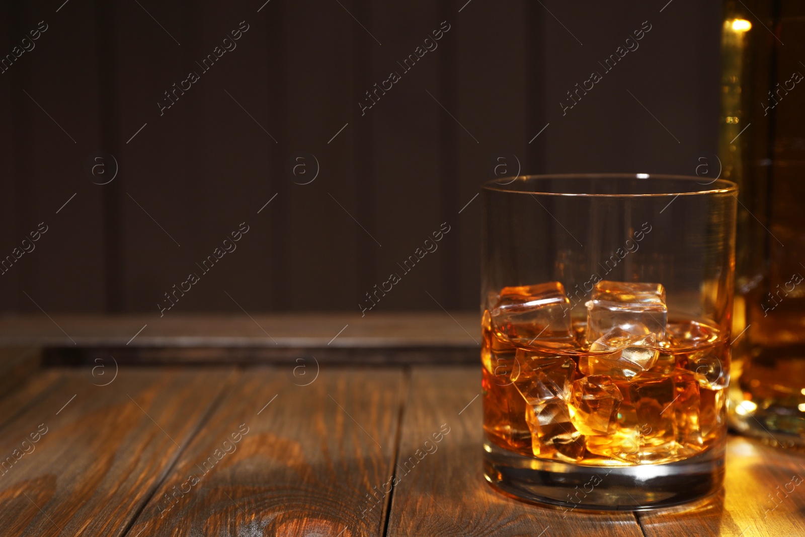 Photo of Whiskey with ice cubes in glass on wooden crate against black background, closeup. Space for text