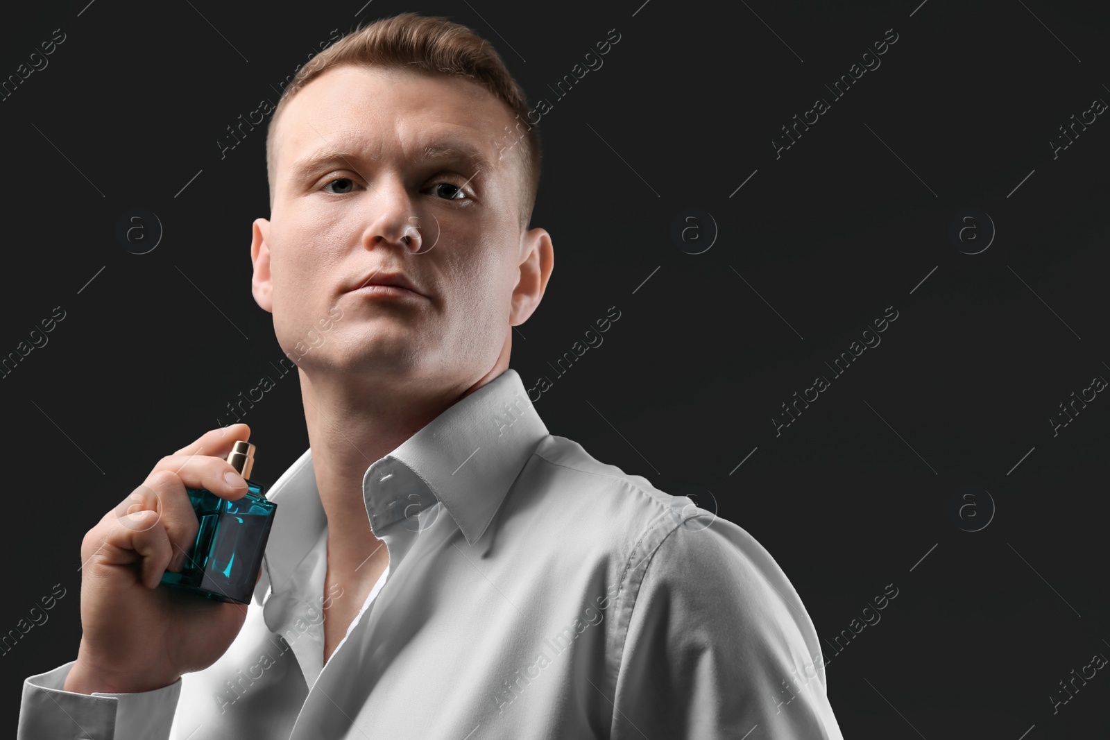 Photo of Handsome man in shirt using perfume on dark background