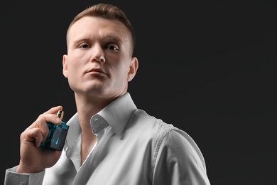 Handsome man in shirt using perfume on dark background