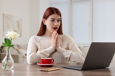 Surprised woman with laptop at wooden table in room