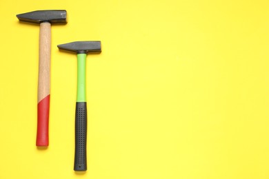 Photo of Two hammers with rubber handles on yellow background, top view. Space for text