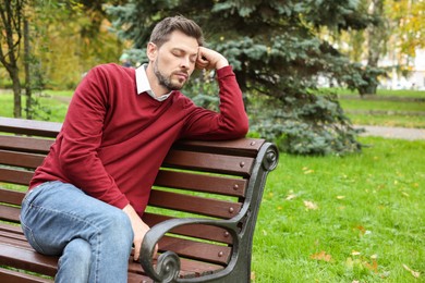 Photo of Tired man sleeping on bench in beautiful green park. Space for text