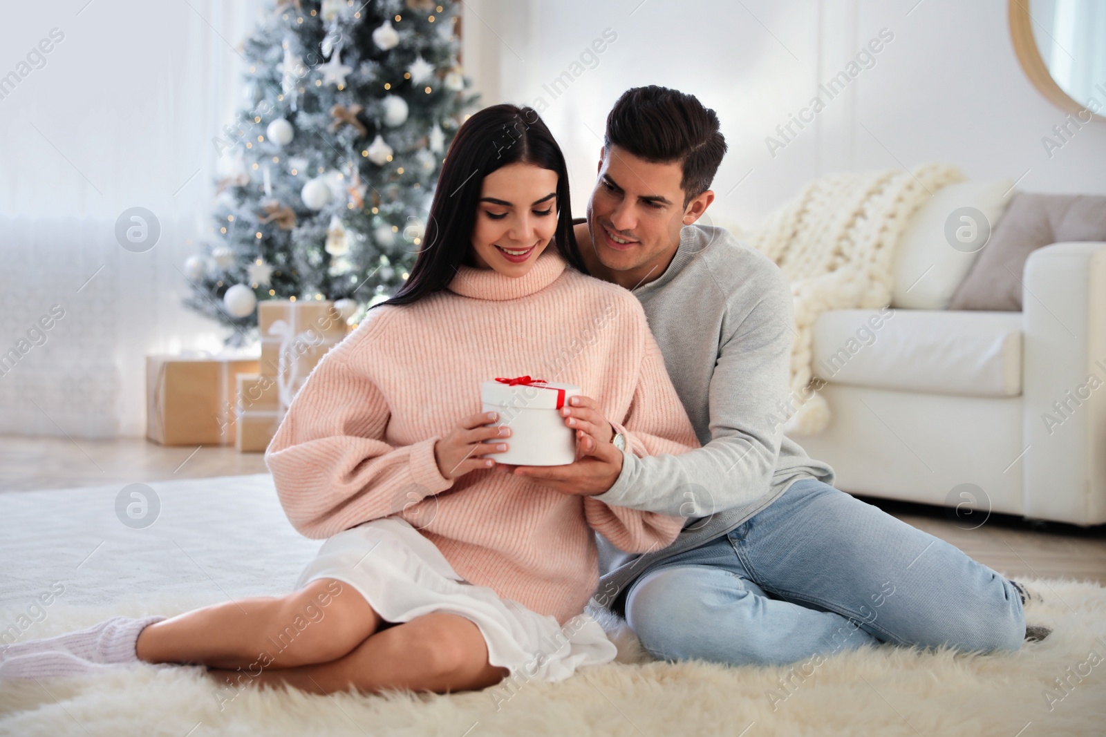 Photo of Couple holding gift box in room with Christmas tree