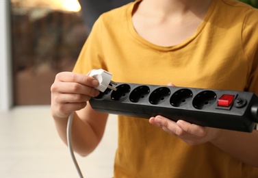 Woman inserting power plug into extension cord indoors, space for text. Electrician's professional equipment