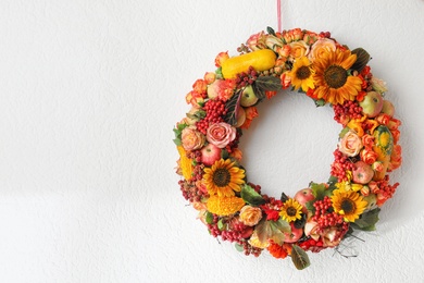 Beautiful autumnal wreath with flowers, berries and fruits hanging on white wall. Space for text