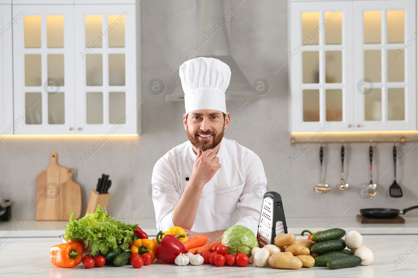 Photo of Portrait of happy professional chef near vegetables at marble table in kitchen