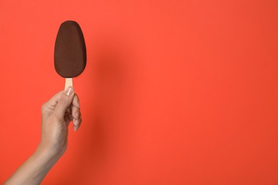 Photo of Woman holding ice cream glazed in chocolate on red background, closeup. Space for text