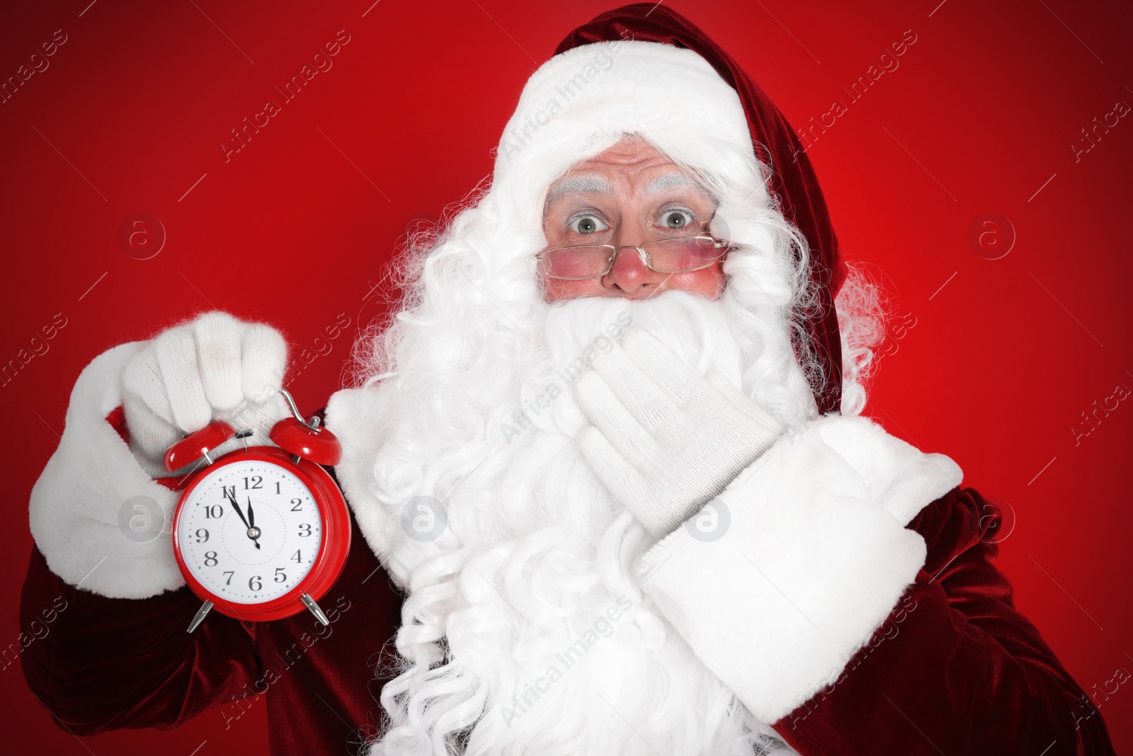 Photo of Santa Claus holding alarm clock on red background. Christmas countdown