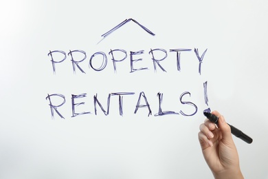 Image of Woman writing exclamation mark in phrase Property Rentals on glass, closeup