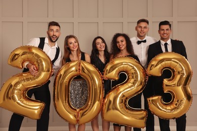 Photo of Happy friends with golden 2023 balloons indoors. New Year celebration