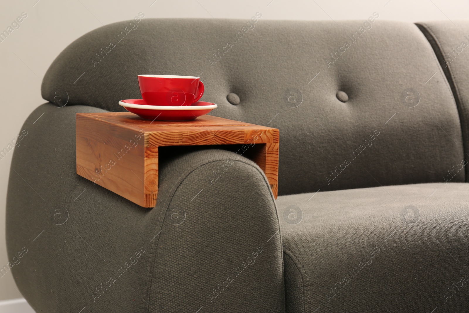 Photo of Cup of tea on sofa with wooden armrest table in room. Interior element