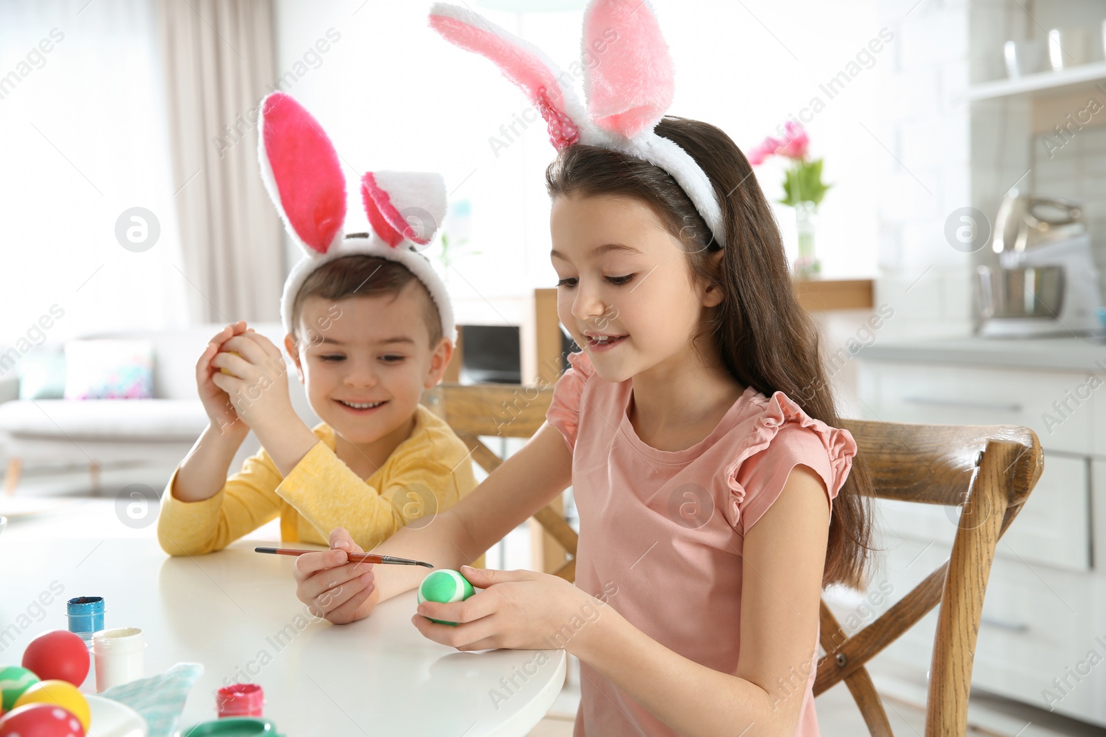 Photo of Cute children with bunny ears headbands painting Easter eggs in kitchen