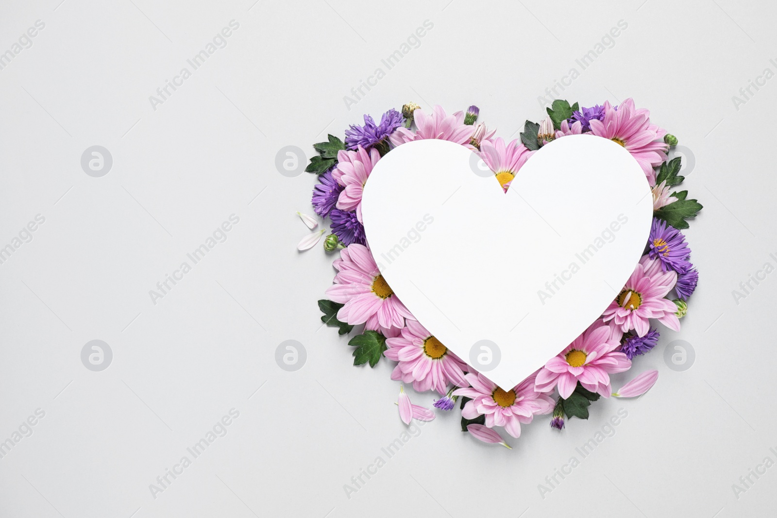 Photo of Beautiful chamomile flowers and heart shaped paper card on white background, top view with space for text