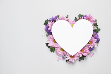 Beautiful chamomile flowers and heart shaped paper card on white background, top view with space for text