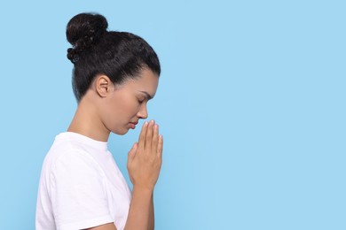 African American woman with clasped hands praying to God on light blue background. Space for text