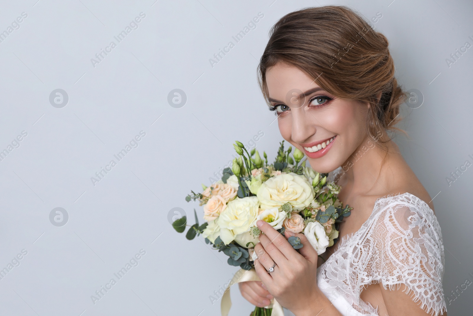 Photo of Young bride with elegant hairstyle holding wedding bouquet on light grey background. Space for text