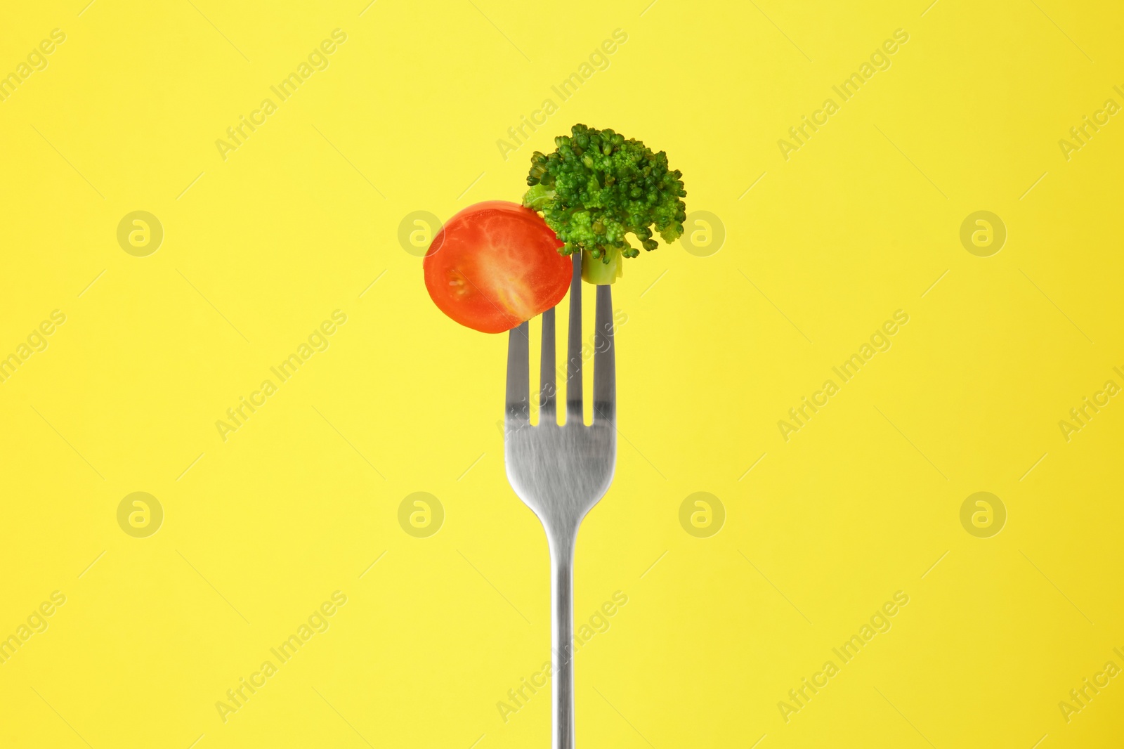 Photo of Fork with half of cherry tomato and broccoli on yellow background