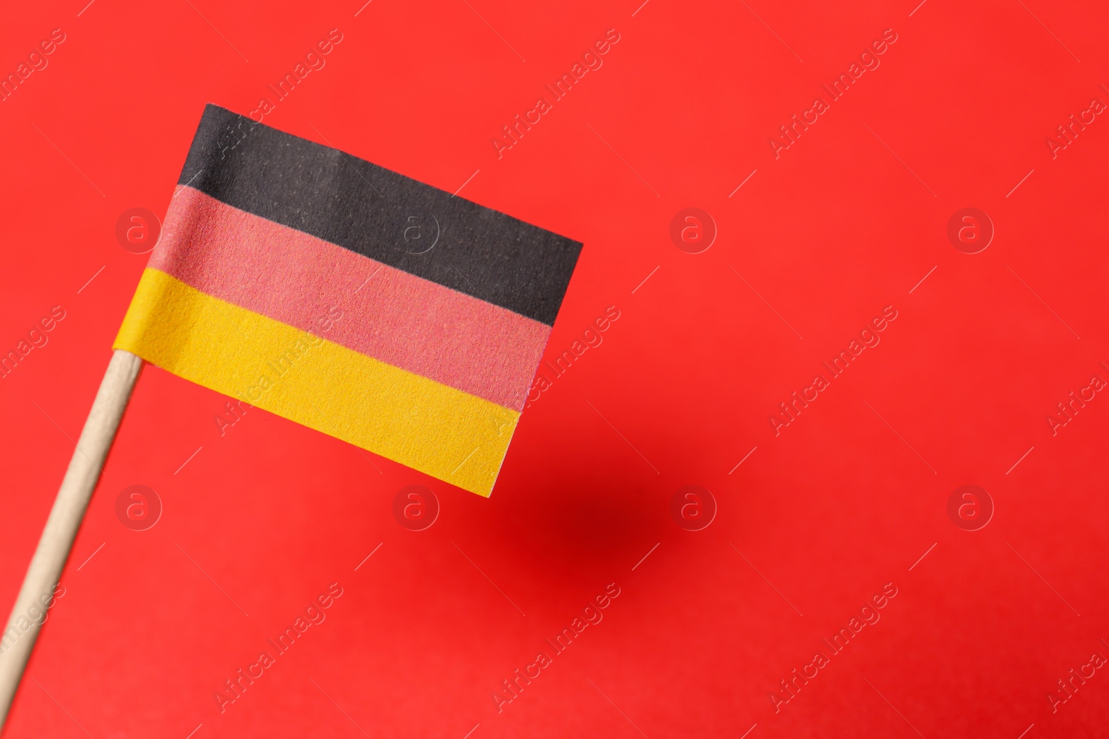 Photo of Small paper flag of Germany on red background, closeup. Space for text