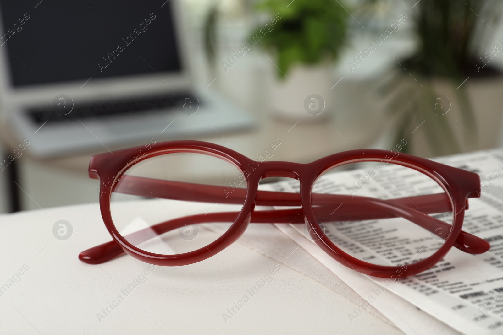 Photo of Glasses and newspaper on armrest indoors, closeup