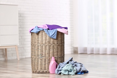 Photo of Laundry basket with dirty clothes and detergent on floor in room, space for text
