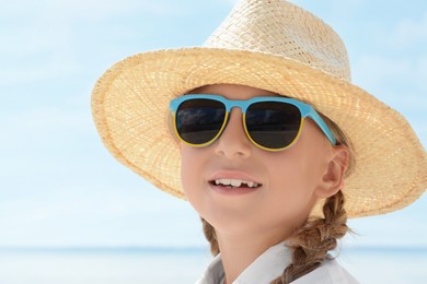 Photo of Little girl wearing sunglasses and hat at beach on sunny day