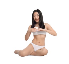 Beautiful young Asian woman holding jar of body cream on white background