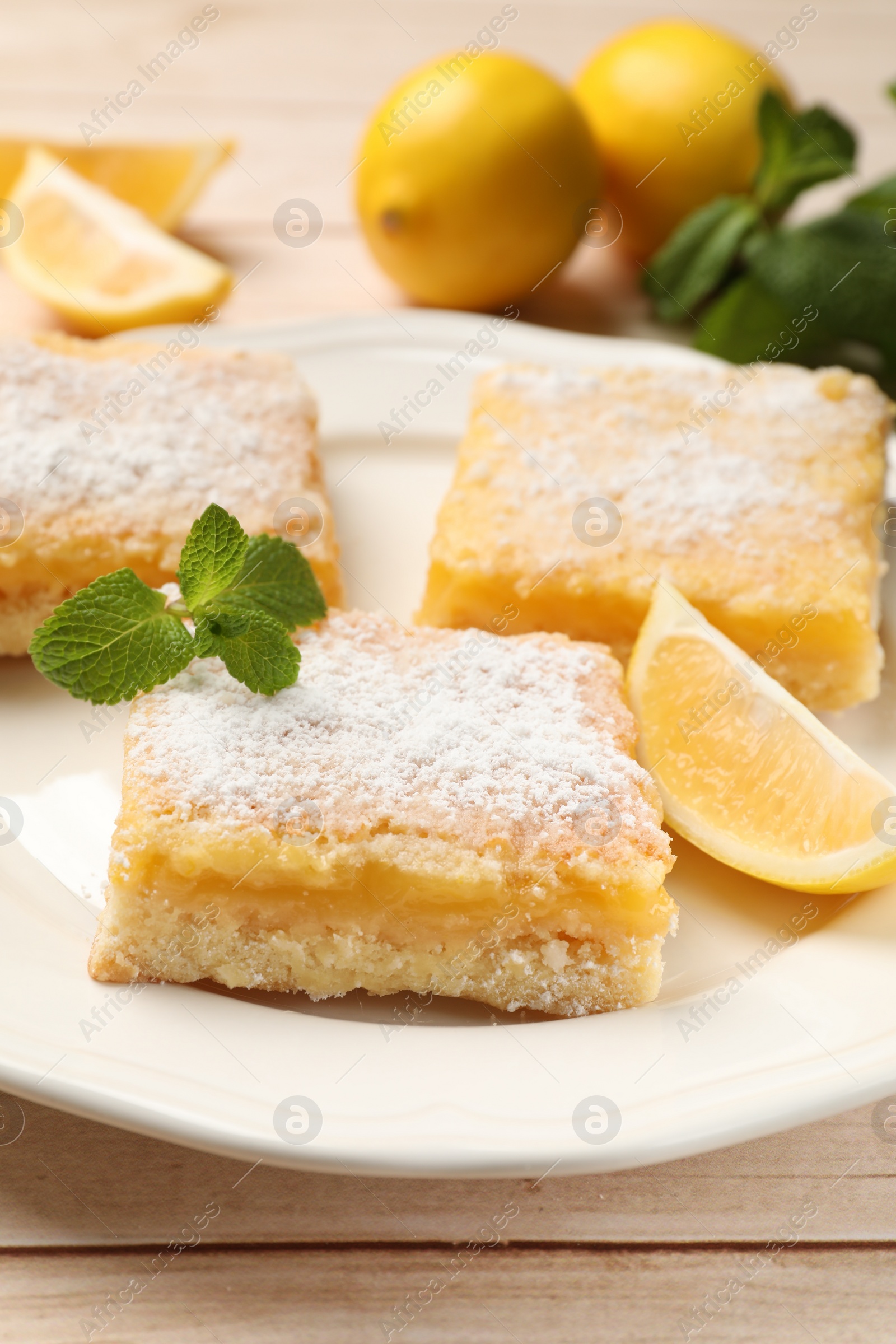 Photo of Tasty lemon bars with powdered sugar and mint on wooden table, closeup