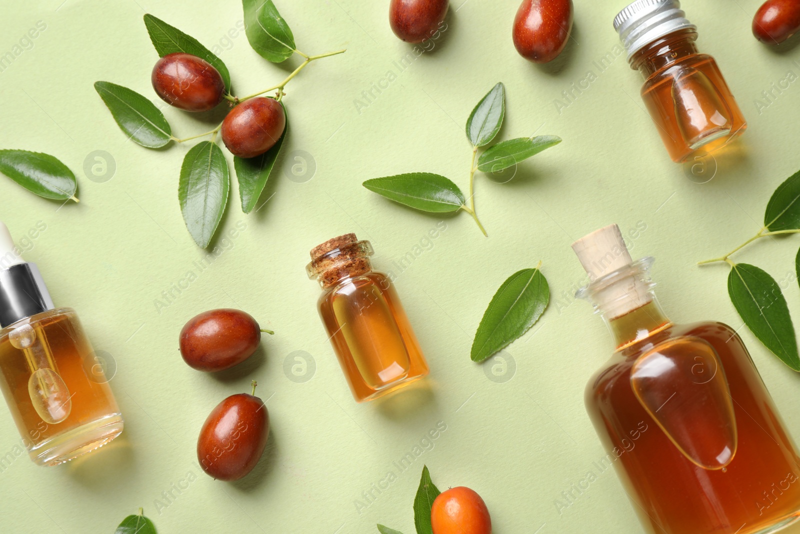 Photo of Glass bottles with jojoba oil and seeds on green background, flat lay