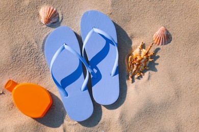 Stylish flip flops, sunscreen and sea shells on beach, flat lay