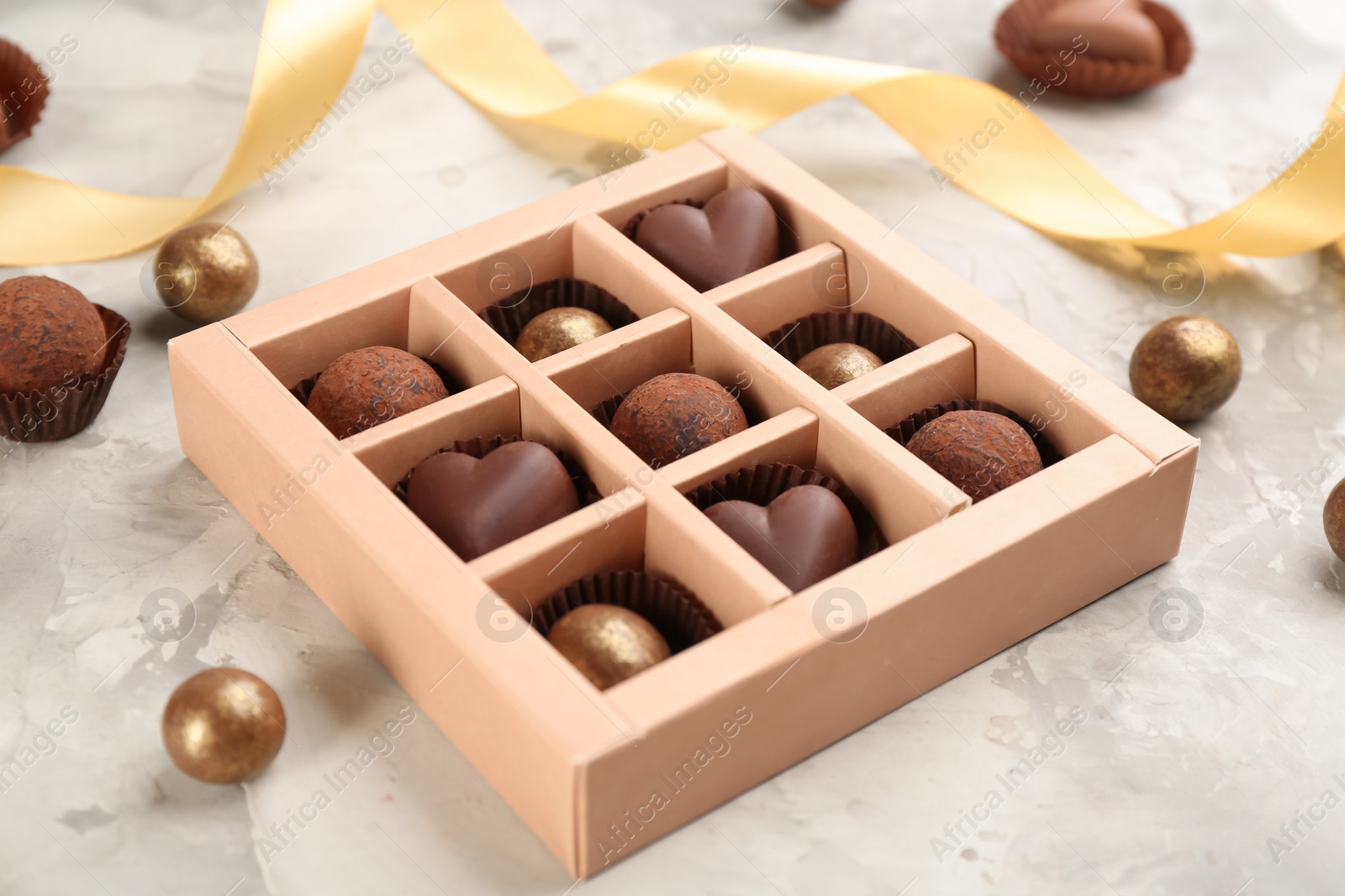 Photo of Different delicious chocolate candies in box on light marble table, closeup