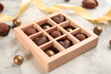 Different delicious chocolate candies in box on light marble table, closeup