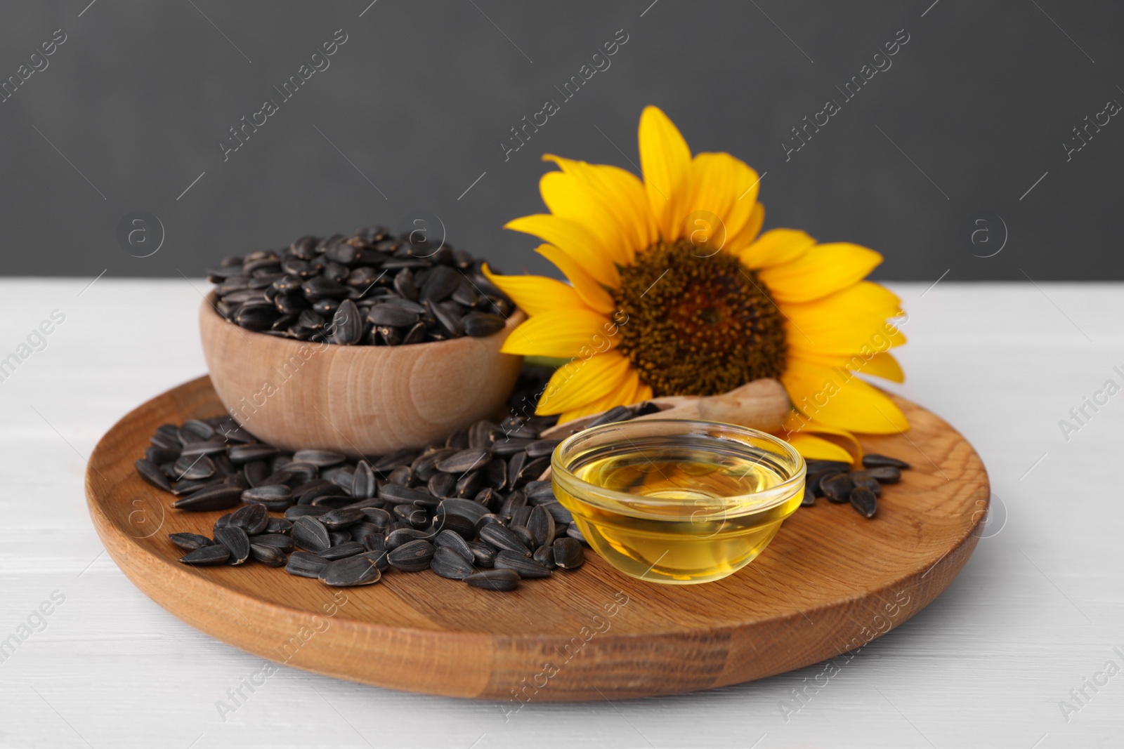 Photo of Sunflower, oil in glass bowl and seeds on white wooden table