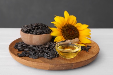 Photo of Sunflower, oil in glass bowl and seeds on white wooden table