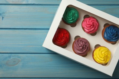 Photo of Box with different cupcakes on light blue wooden table, top view
