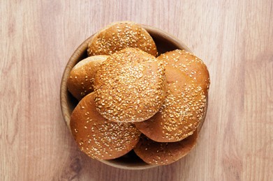 Photo of Bowl of fresh buns with sesame seeds on wooden table, top view