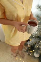 Photo of Woman with cup of tea near Christmas tree indoors, closeup