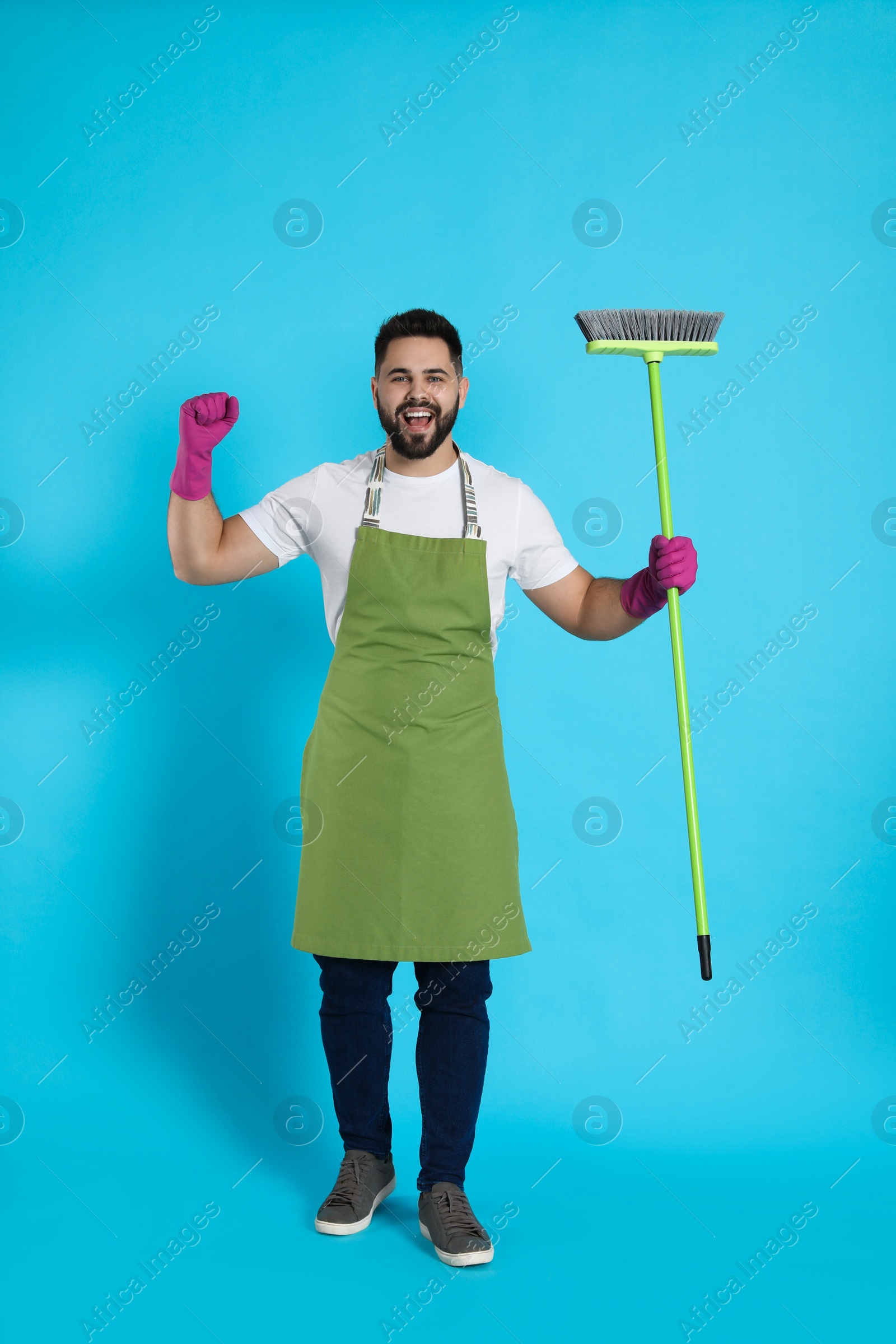 Photo of Young man with green broom on light blue background