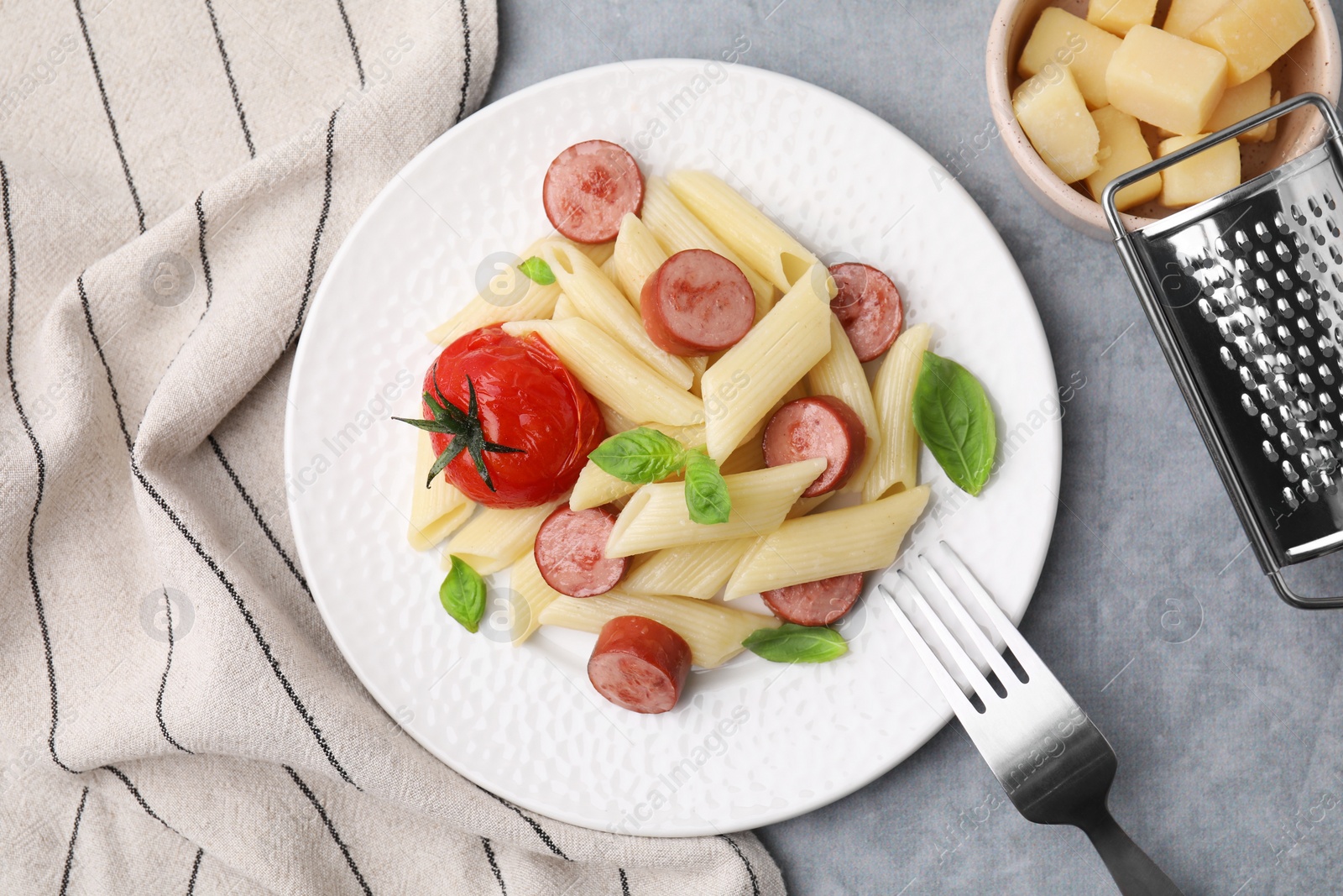 Photo of Tasty pasta with smoked sausage, tomato and basil served on light grey table, flat lay