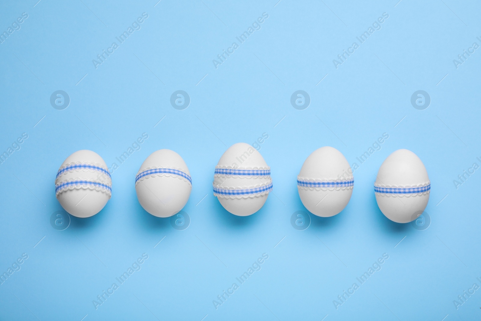 Photo of Beautifully decorated Easter eggs on light blue background, flat lay