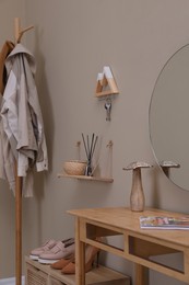 Modern hallway interior with stylish furniture, table and wooden hanger for keys on beige wall